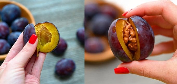 A hand with red nail polish shows how to remove the pit from a blue Italian plum (left) and stuff the cavity with a whole raw walnut (right) for roasted plums.