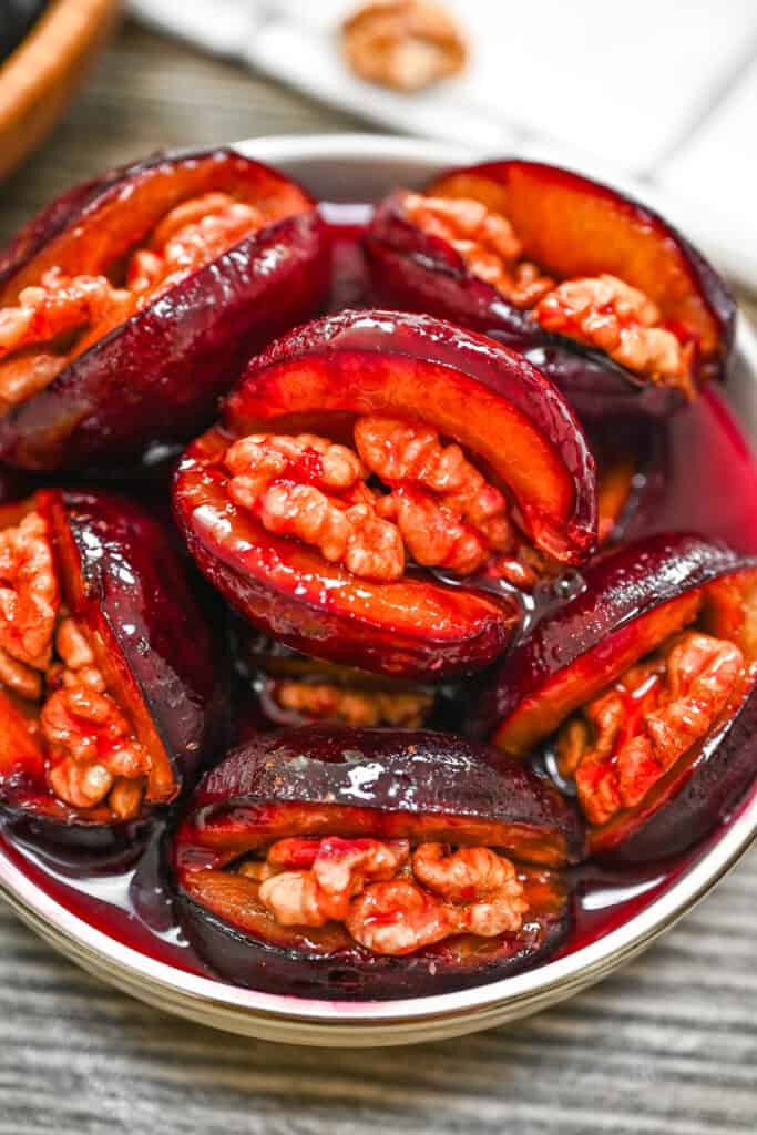4-ingredient roasted plums stuffed with walnuts in a ceramic bowl with glossy syrup