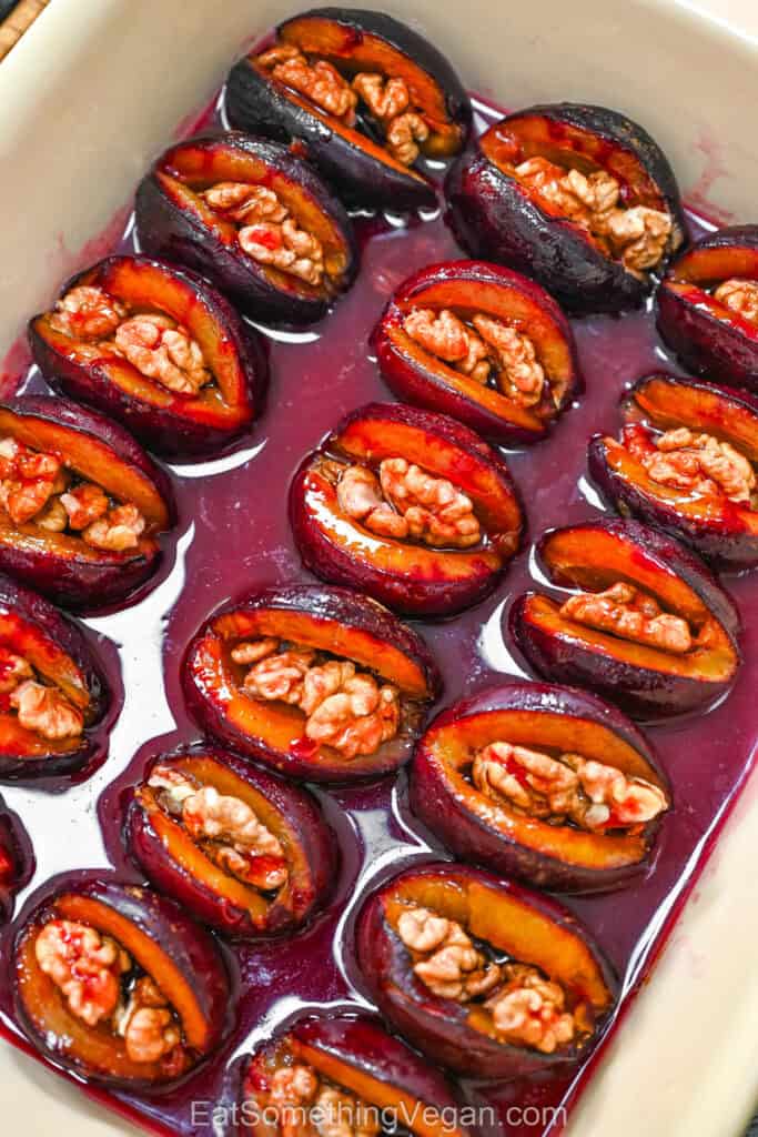 4-Ingredient Roasted Plums with Walnuts in a ceramic baking dish with glossy syrup