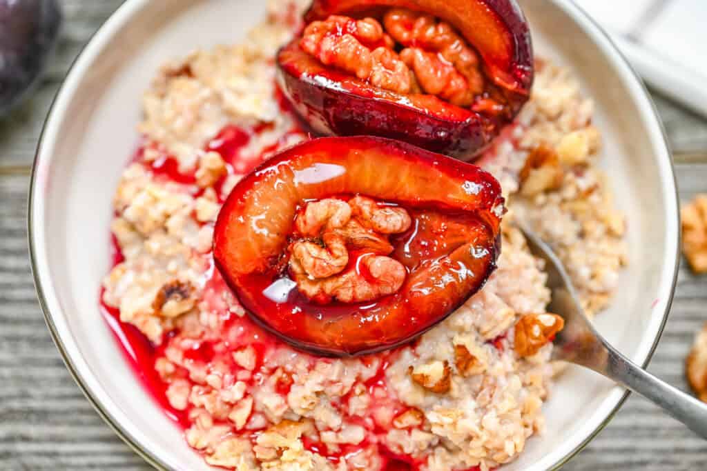 A bowl of oatmeal topped with roasted walnut-stuffed plums and plum syrup