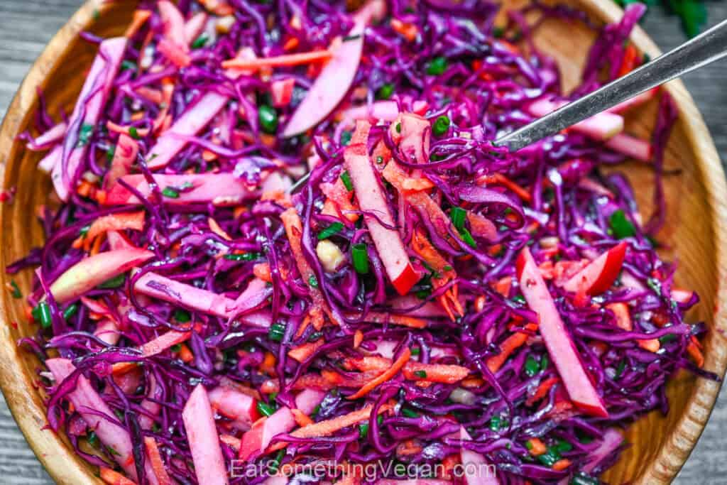 Fresh colorful cabbage salad in a wooden bowl with a metal serving fork.