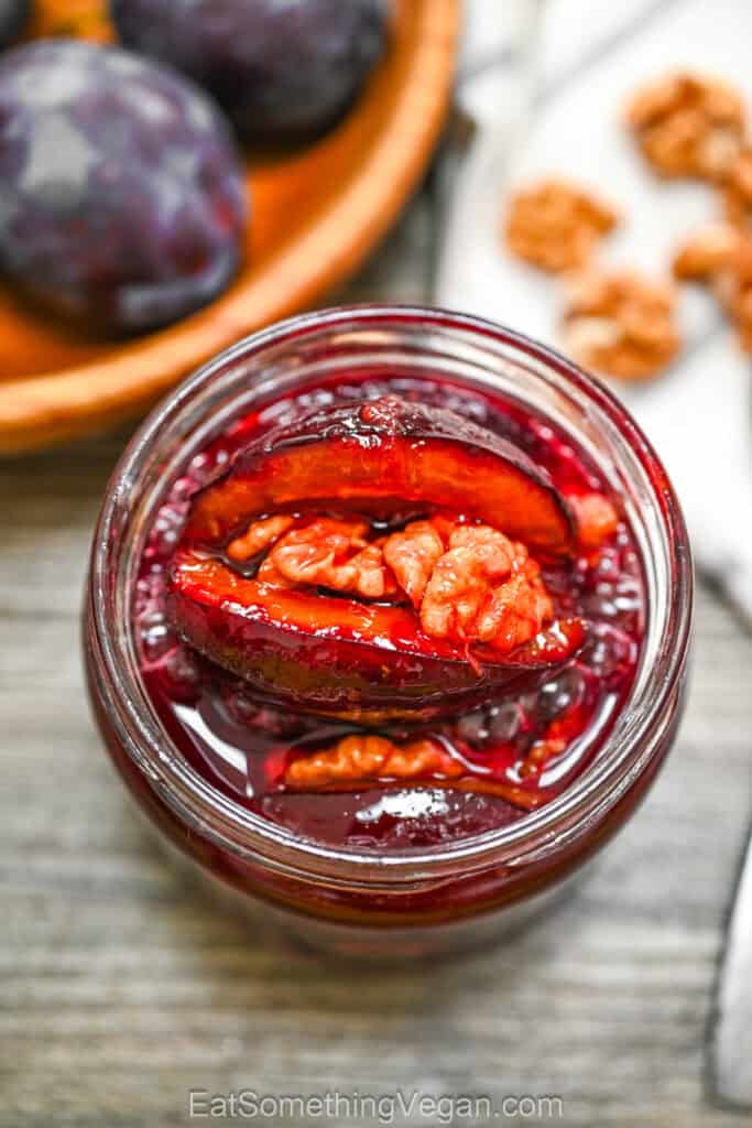 4-Ingredient Roasted Plums with Walnuts stored in a glass jar with rich syrup