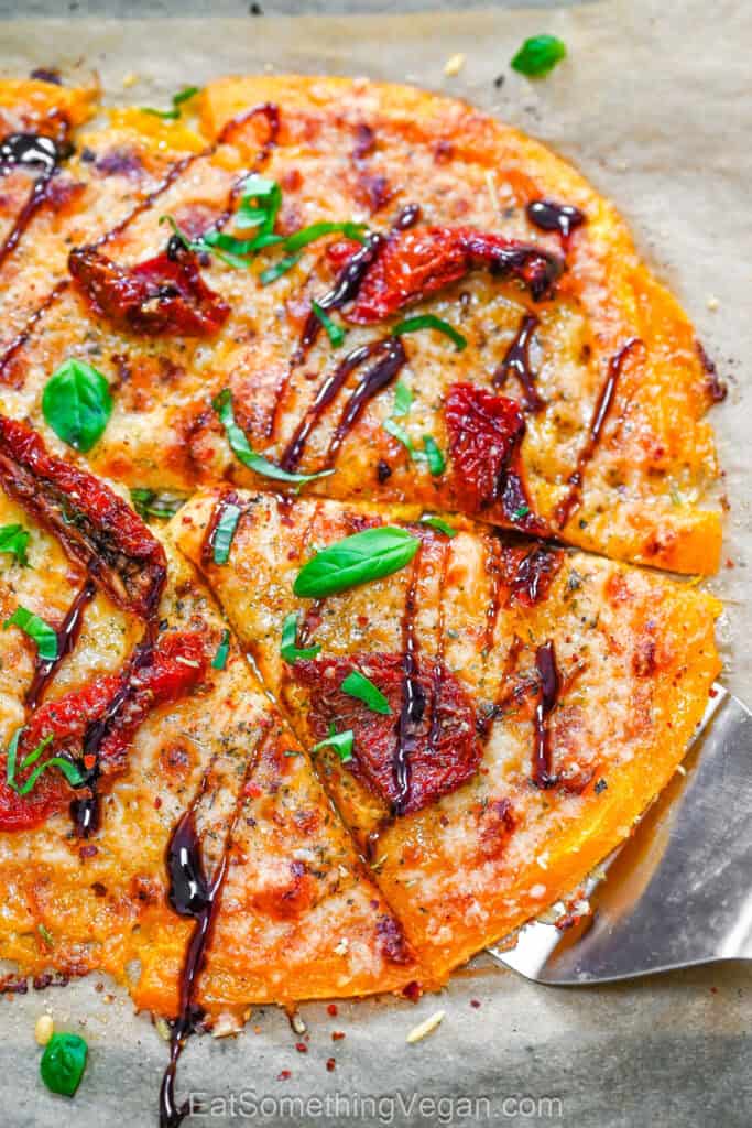 Smashed Butternut Squash Pizza baked on parchment paper, topped with dairy-free mozzarella, savory sun-dried tomatoes, fresh basil, and a generous balsamic glaze drizzle.