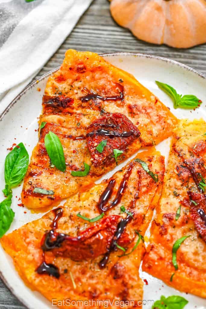 Smashed Butternut Squash Pizza slices served on a white plate, topped with sun-dried tomatoes, fresh basil leaves, and balsamic glaze.