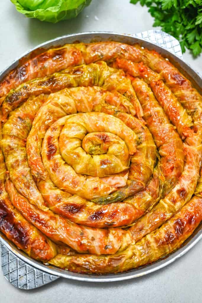 Golden baked spiral cabbage rolls arranged in a round baking dish with crisp caramelized edges.