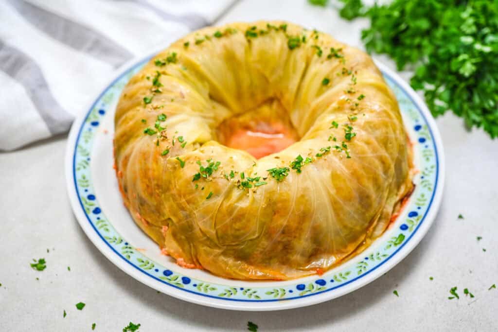 A whole baked Bundt pan cabbage roll cake on a round serving platter, garnished with fresh chopped parsley