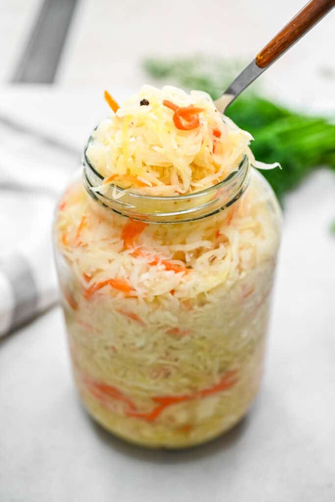 Crunchy homemade sauerkraut packed in a glass jar topped with shredded cabbage, carrots, and black peppercorns.