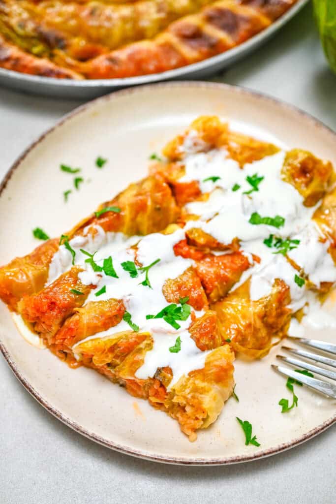 A tender wedge of baked spiral cabbage rolls served on a plate, topped with creamy dairy-free sour cream and fresh parsley.