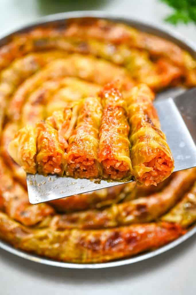 A slice of baked spiral cabbage roll lifted on a spatula, showing the tender leaves and savory seasoned rice filling inside.