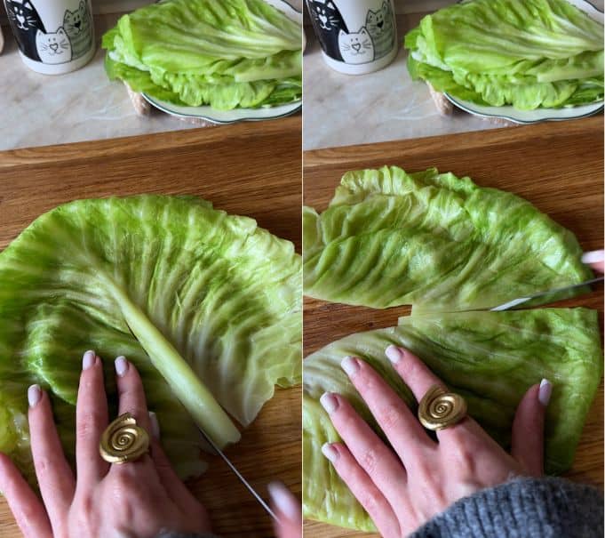 Trimming the thick center stem from a softened green cabbage leaf and slicing it into two halves on a wooden cutting board for spiral cabbage rolls.