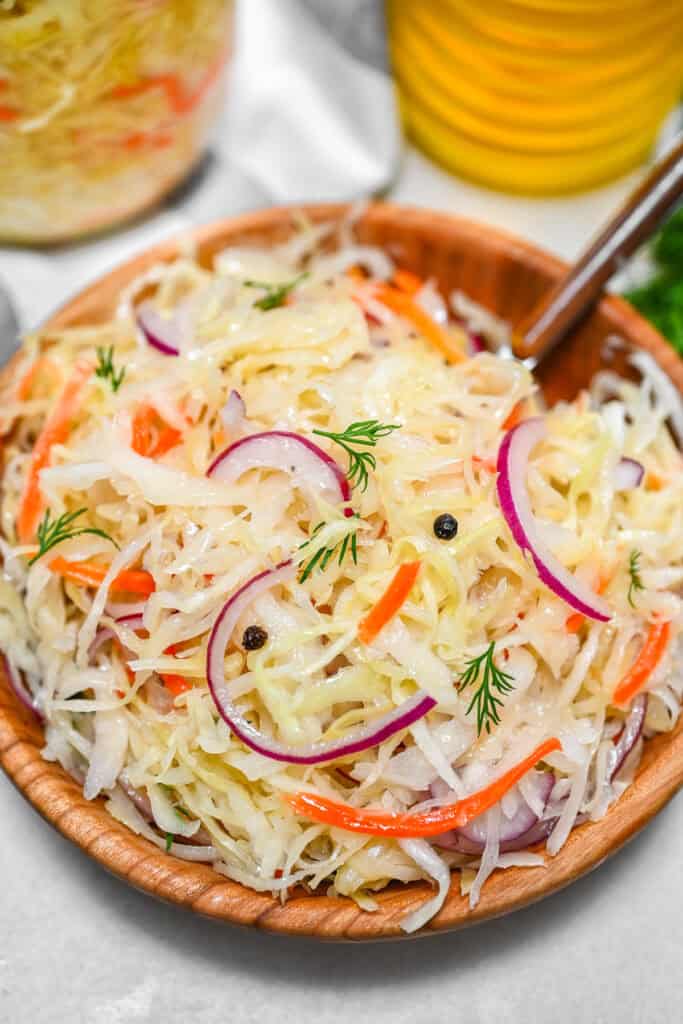 Crunchy sauerkraut salad mixed with sliced red onions, fresh dill, and sunflower oil in a rustic wooden bowl.